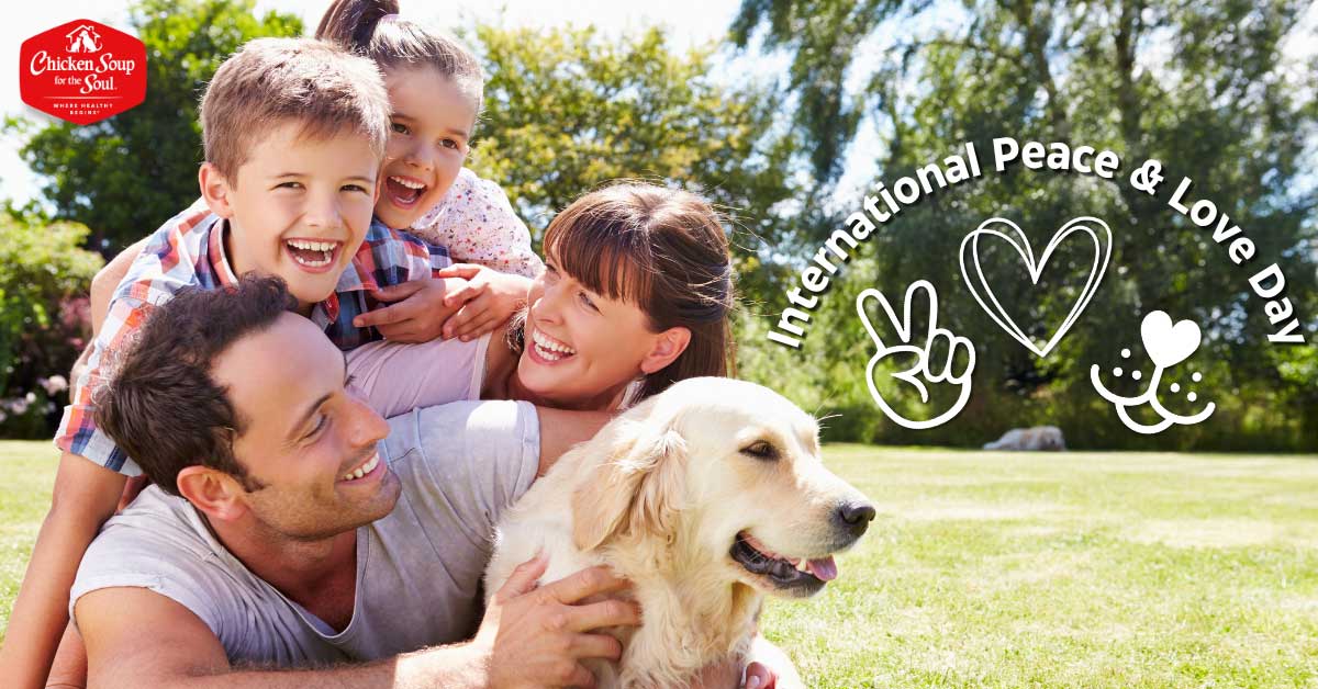 two children, a woman and man grin and huddle around a retriever dog on a green lawn